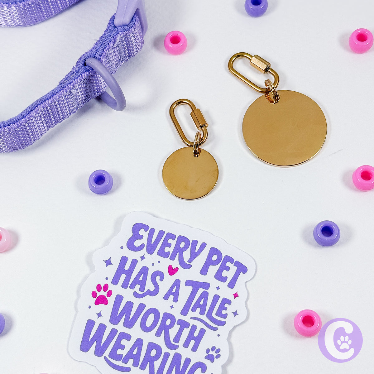 Gold pet tags, purple and pink beads, and a sticker with text on a white background