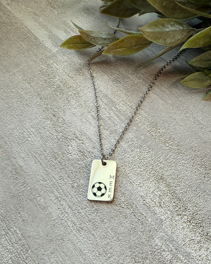 Necklace with a rectangular tag featuring a soccer ball design on a textured surface.