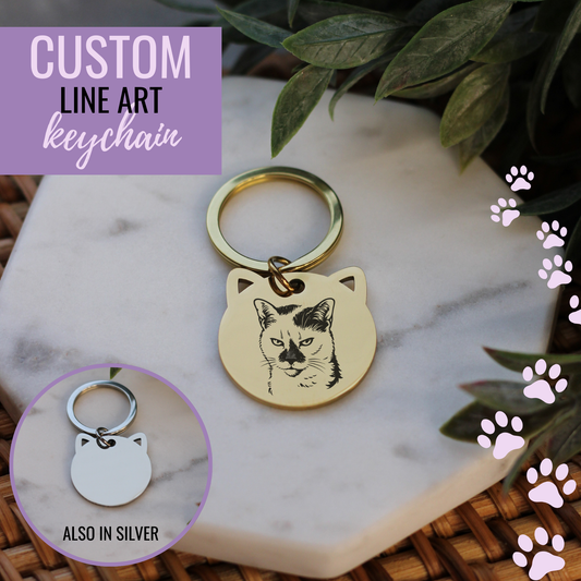 Gold keychain with cat design on a marble surface with green leaves.