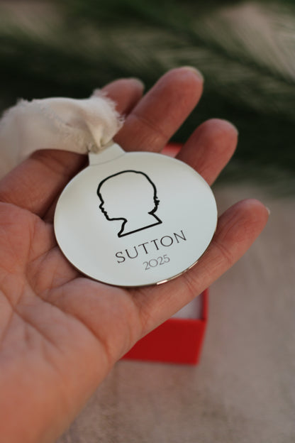 Hand holding a round ornament with 'Sutton' and a silhouette.