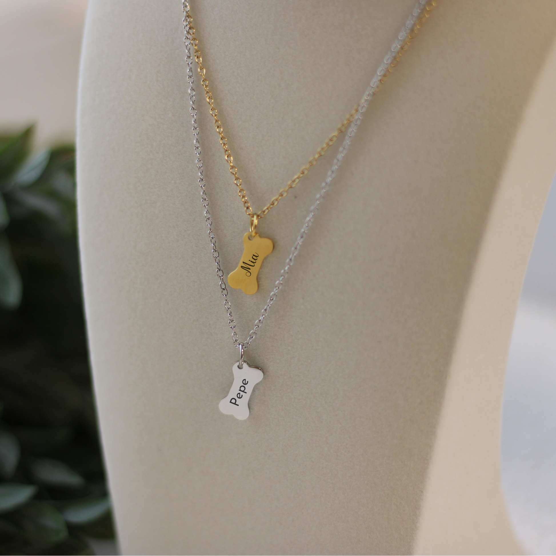 Two necklaces with dogbone charms on a mannequin bust.