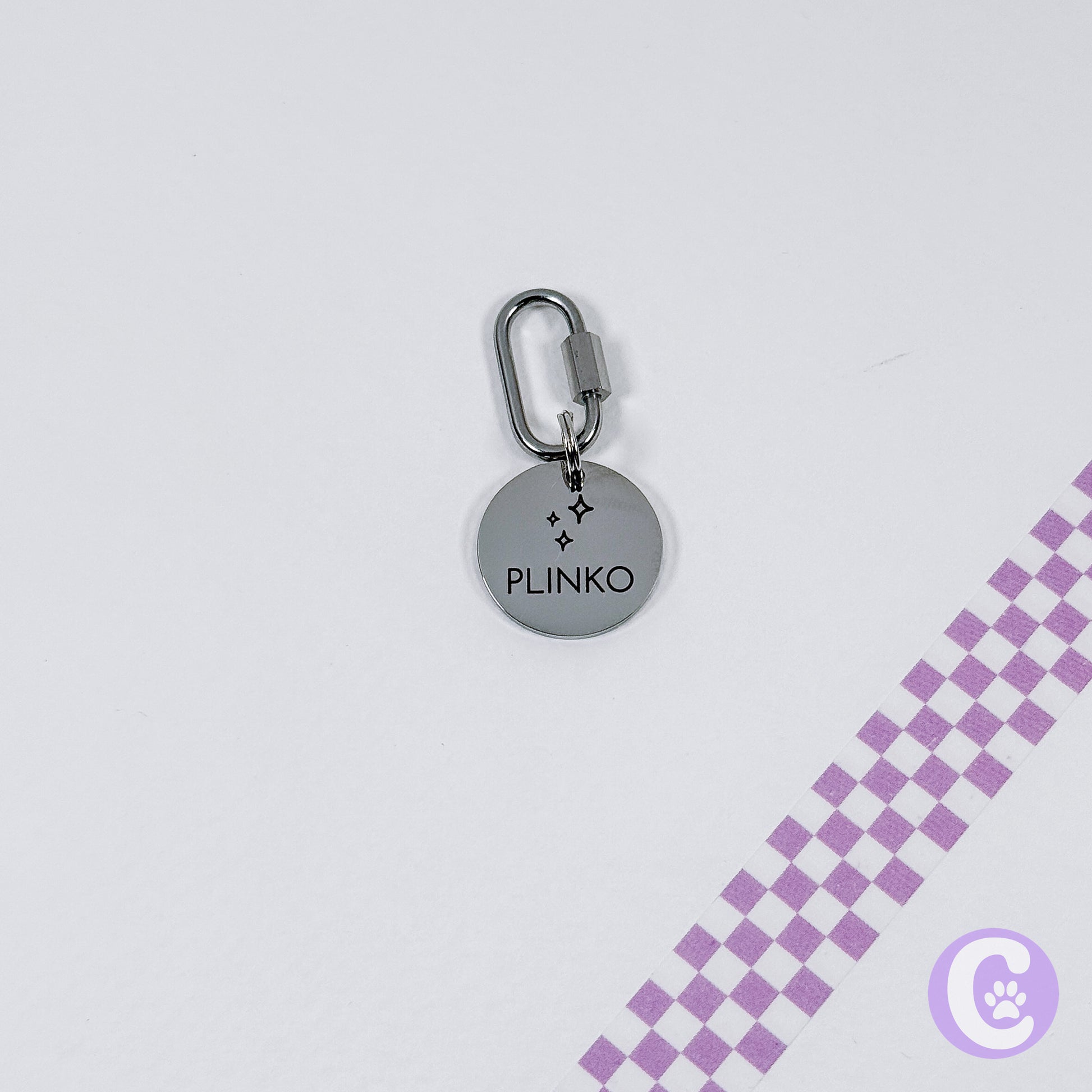Round metallic keychain with 'Plinko' branding on a light gray background
