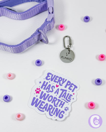 Purple pet collar with a tag, pink and purple beads, and a 'Every Pet Has a Tale Worth Wearing' sticker on a white background.