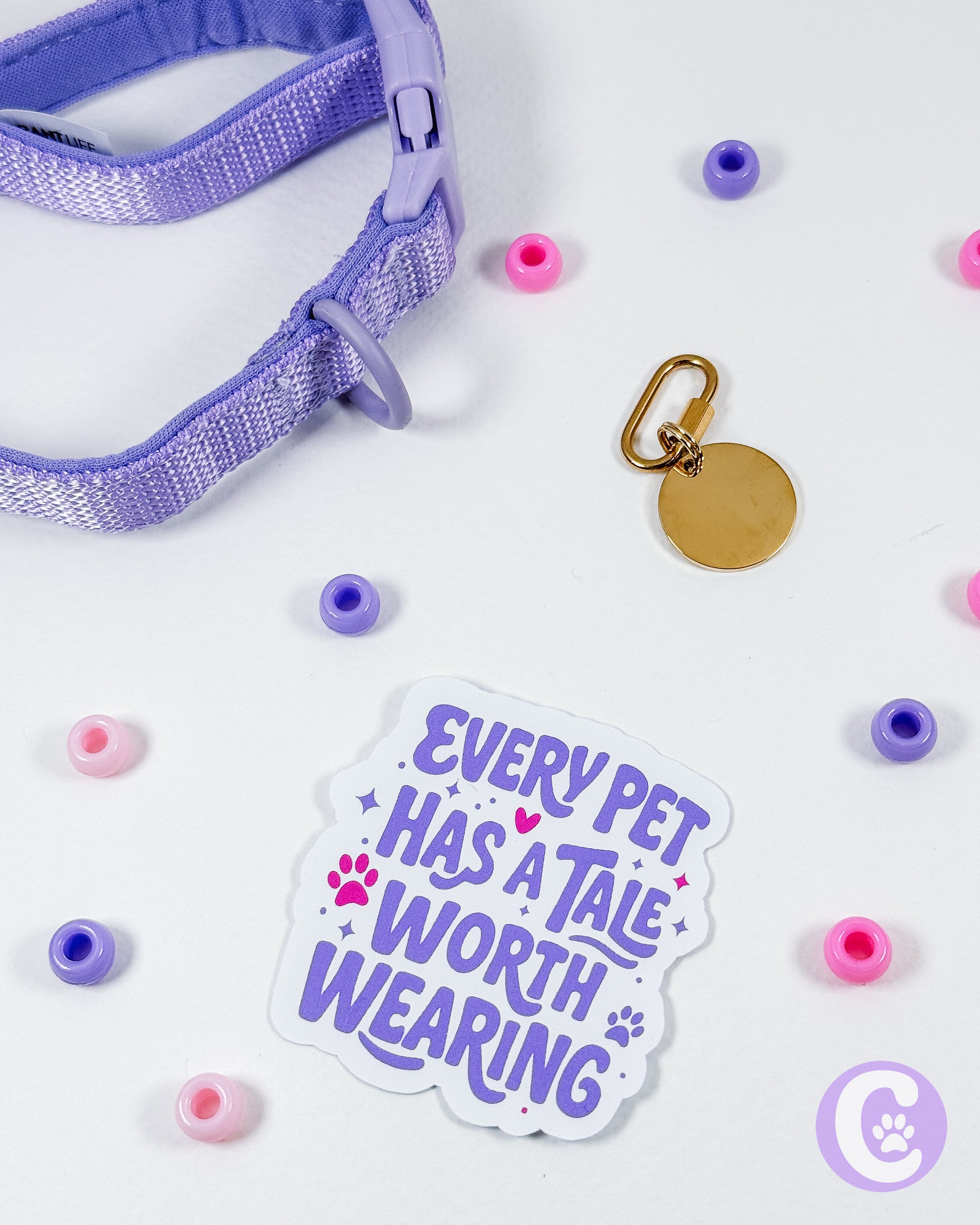 Purple pet collar with decorative beads and a gold tag, accompanied by a 'Every pet has a tale worth wearing' sticker on a white background.