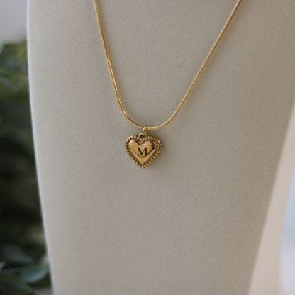 Gold heart-shaped necklace with a 'M' pendant on a neutral background