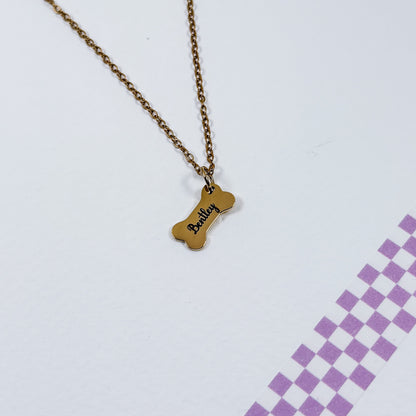 Gold necklace with a bone-shaped pendant on a light purple background