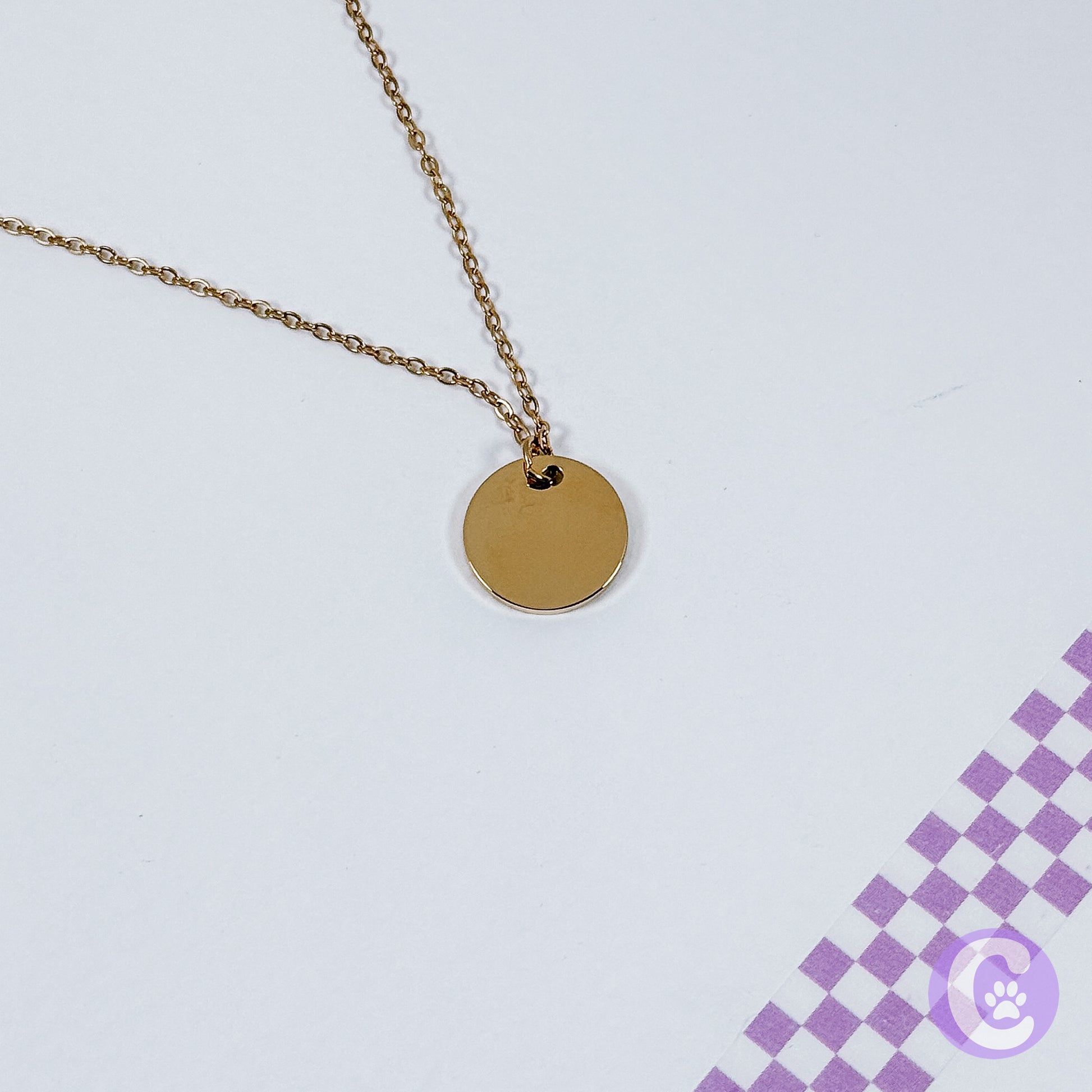 Gold necklace with a round pendant on a light gray background