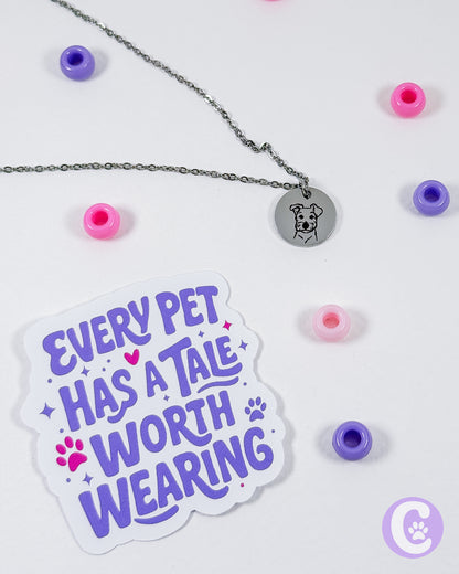 Sticker with 'Every pet has a tale worth wearing' text, necklace with pendant, and colorful beads on a white background.