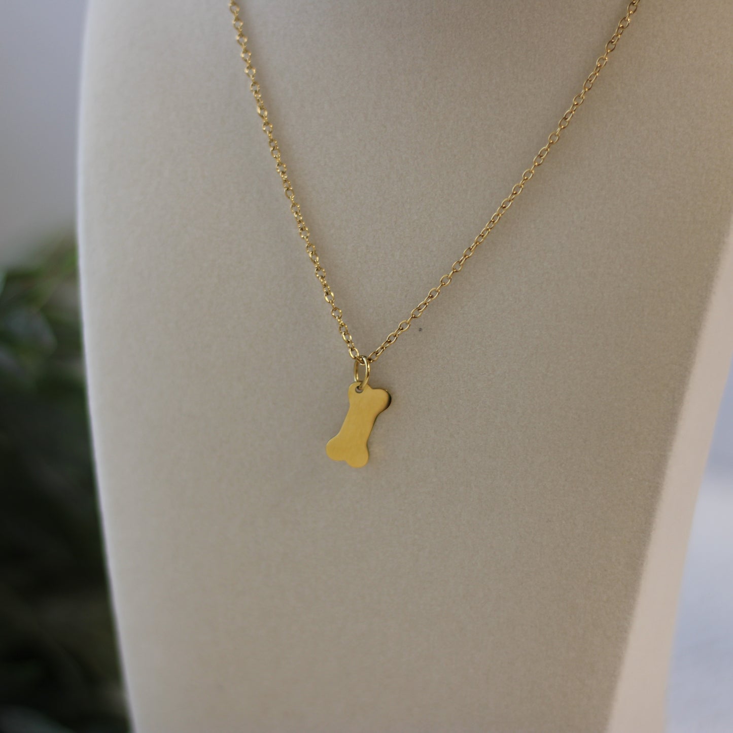 Gold necklace with a bone-shaped pendant on a mannequin.