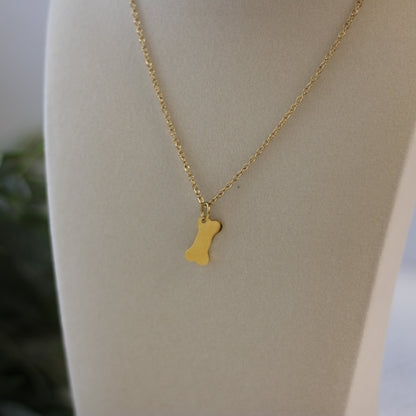 Gold necklace with a bone-shaped pendant on a mannequin.