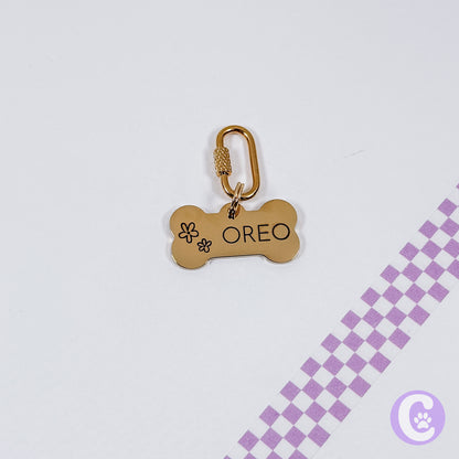 Gold bone-shaped pet tag with 'OREO' engraved on a light gray background