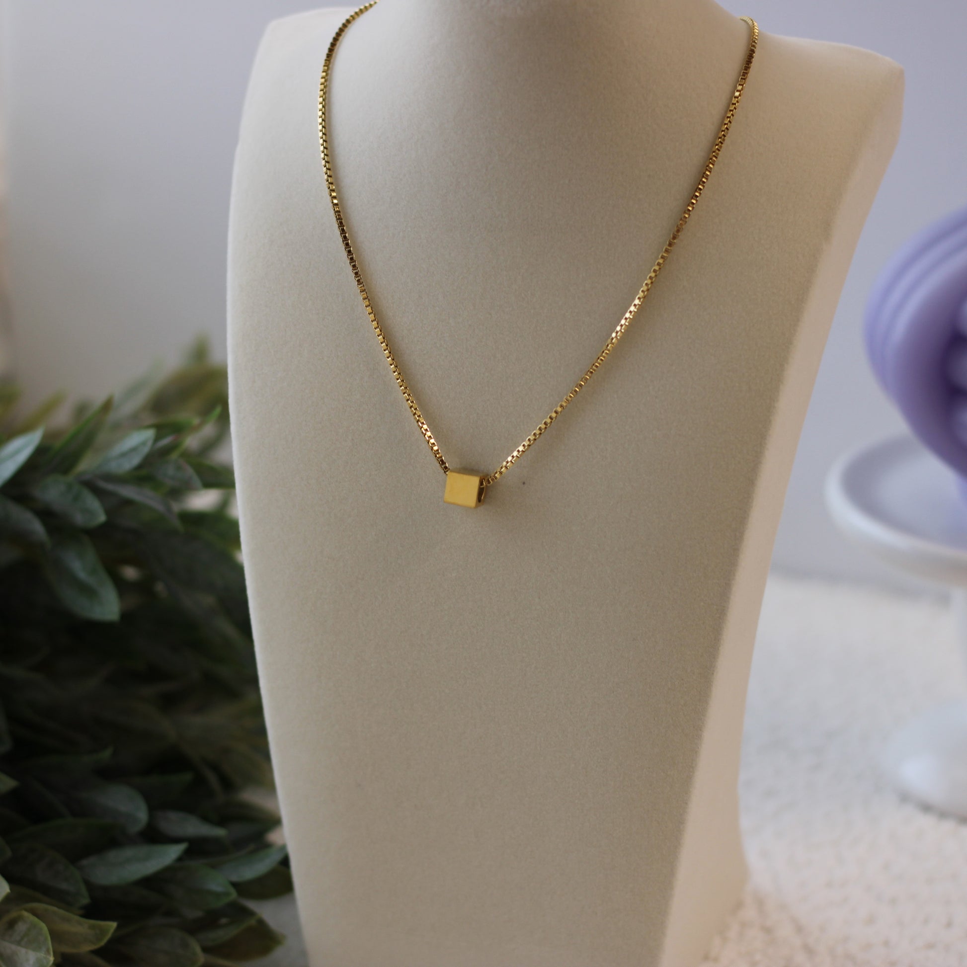 Gold necklace with a square pendant on a mannequin bust.