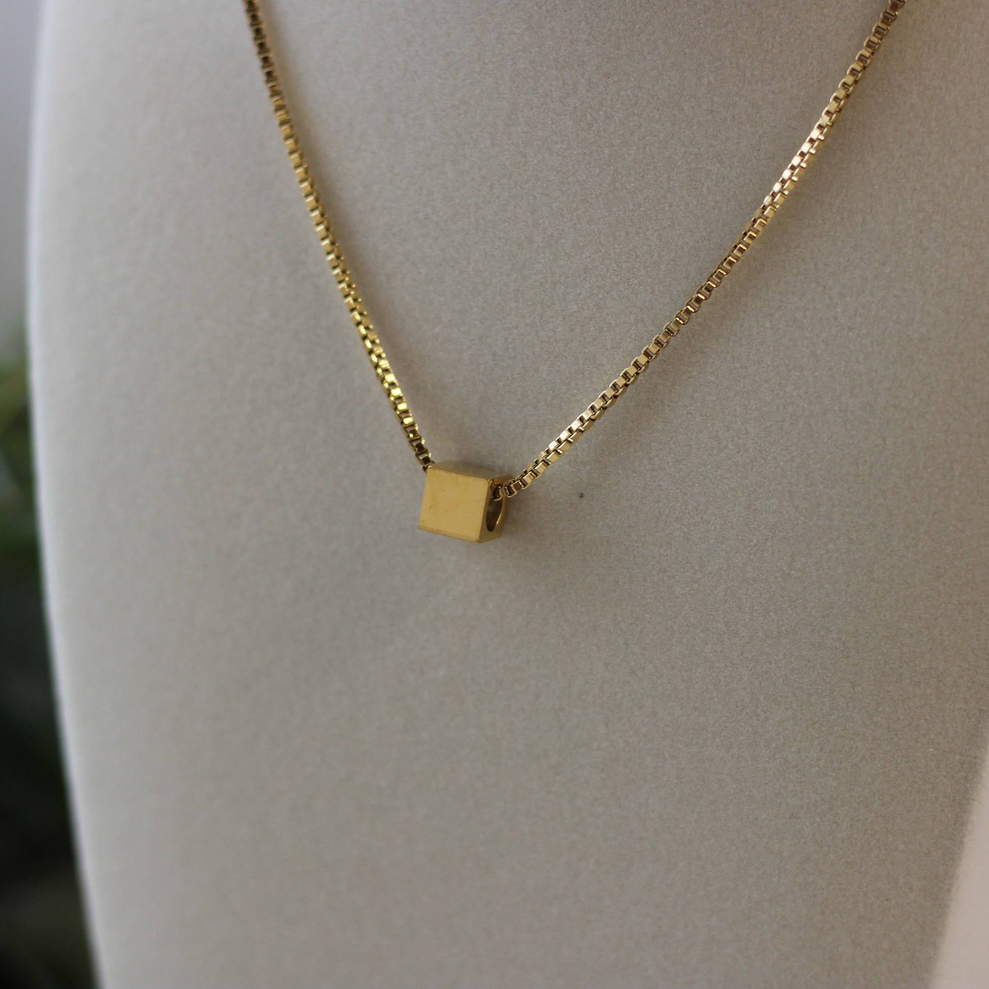 Gold necklace with a square pendant on a white mannequin bust.