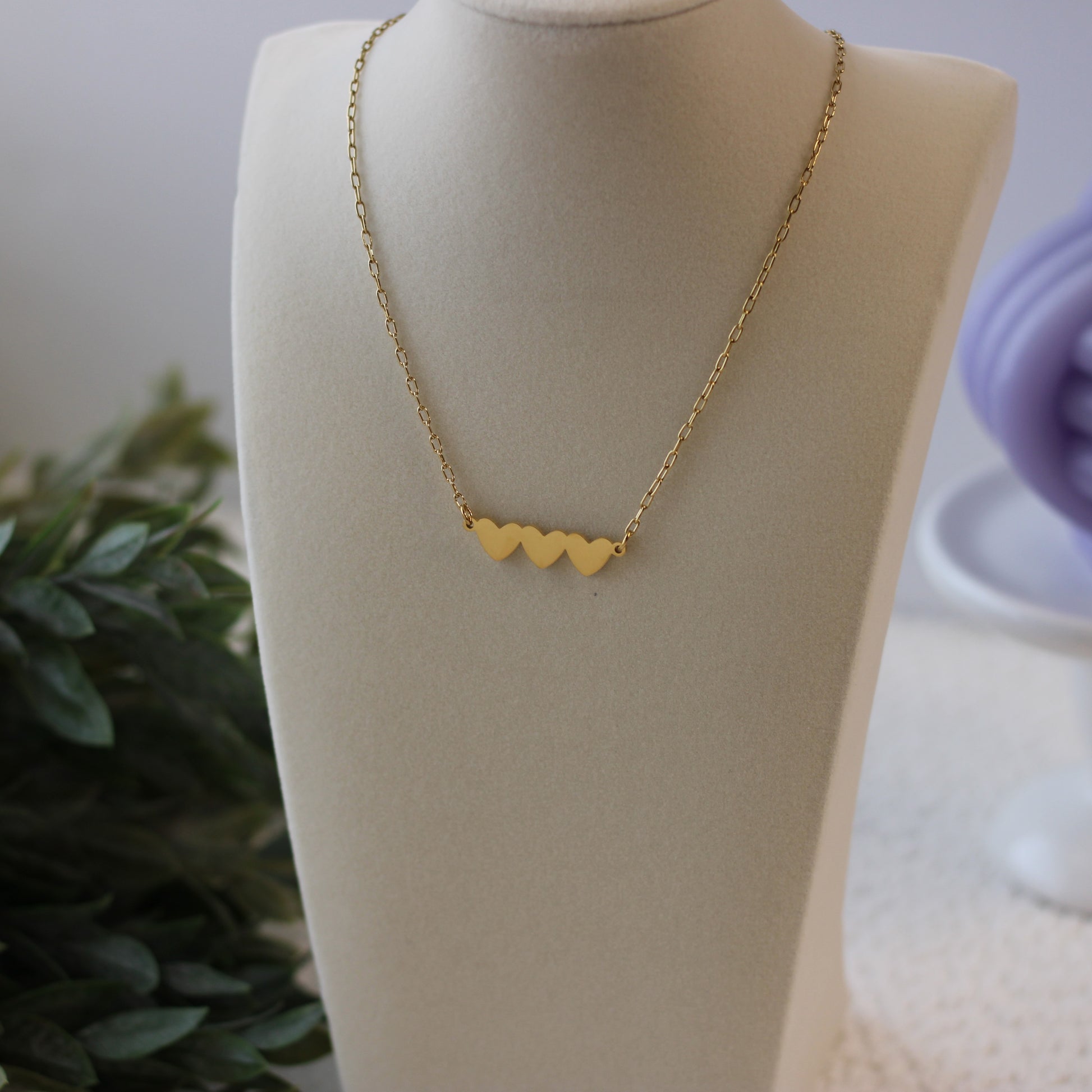 Gold necklace with heart-shaped pendants on a mannequin bust.