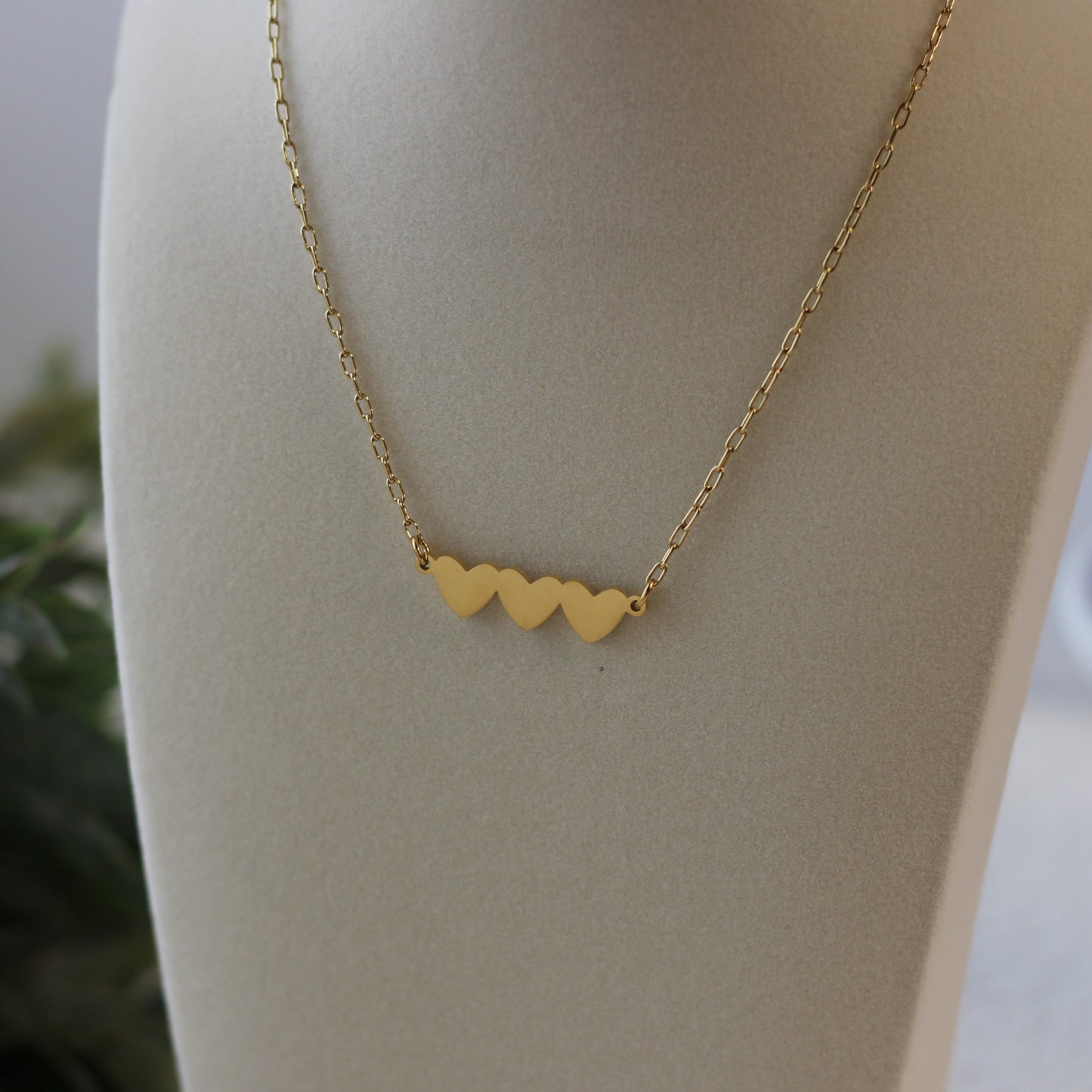 Gold necklace with heart-shaped pendants on a mannequin bust.
