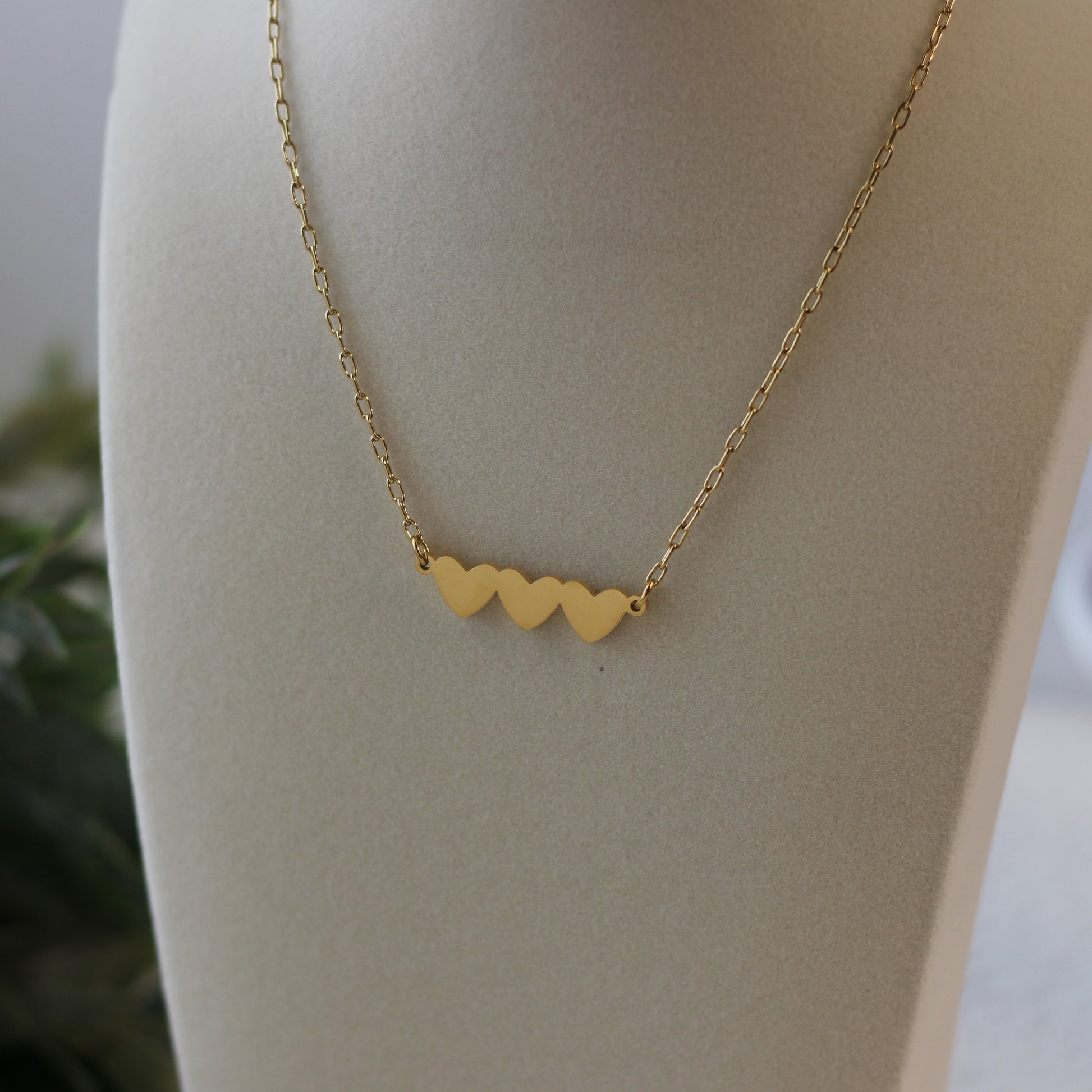 Gold necklace with heart-shaped pendants on a mannequin bust.