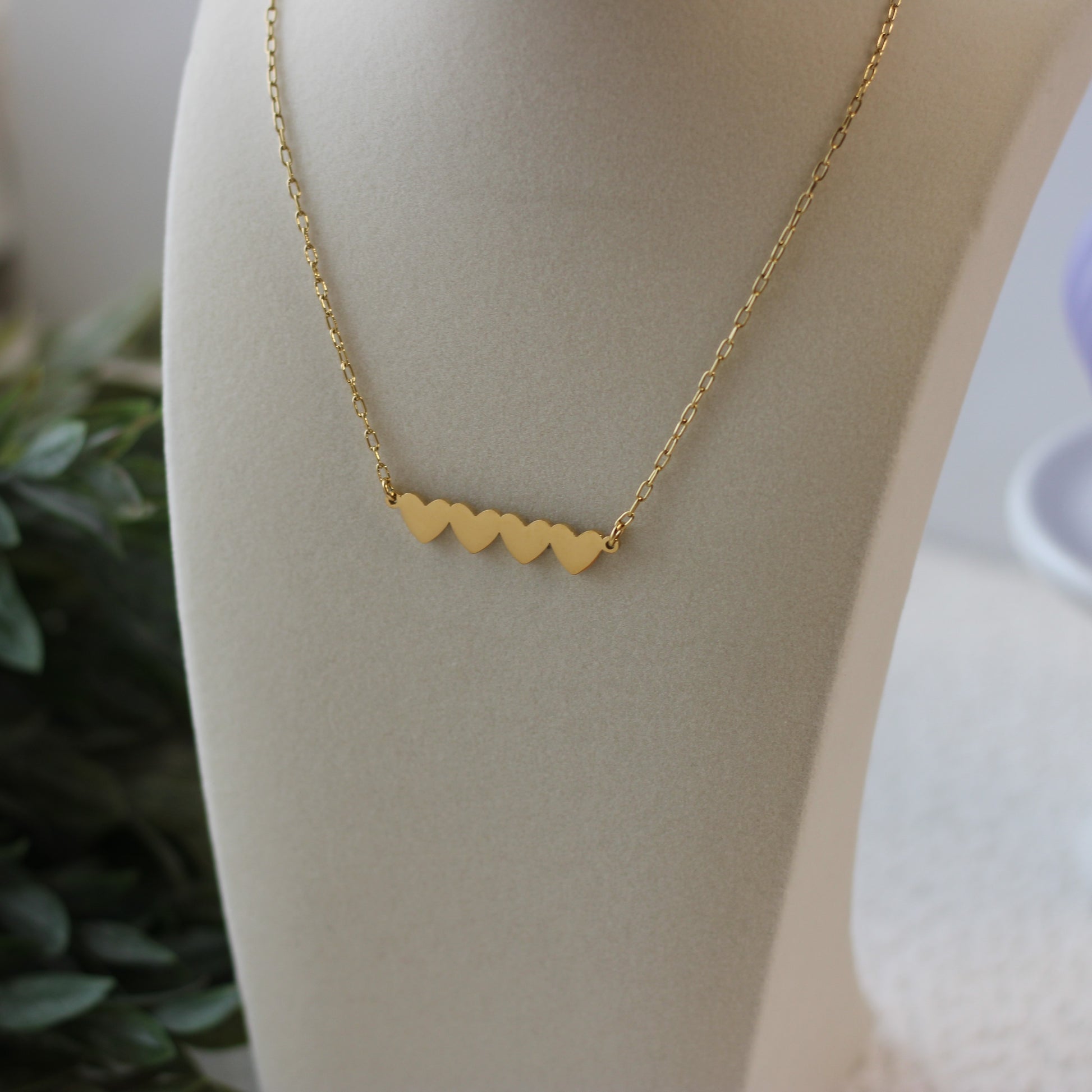 Gold necklace with heart-shaped pendants on a mannequin bust.