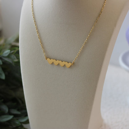 Gold necklace with heart-shaped pendants on a mannequin bust.
