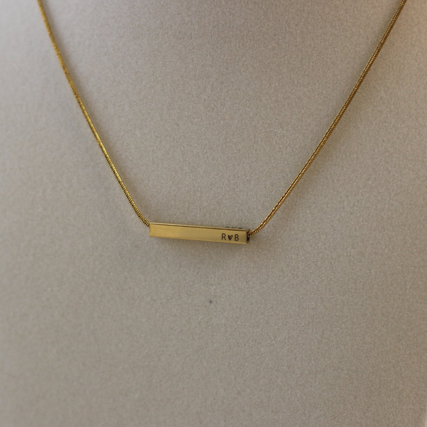 Gold necklace with a bar pendant on a beige background