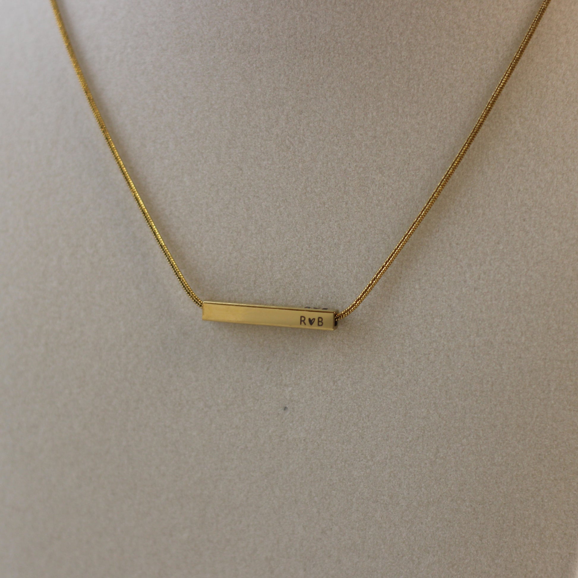 Gold necklace with a bar pendant on a beige background