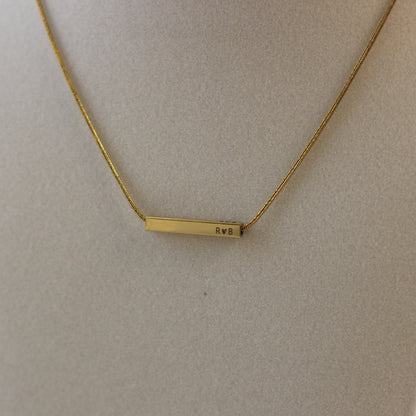 Gold necklace with a bar pendant on a beige background