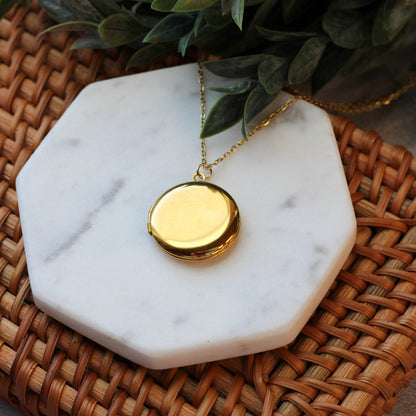Gold necklace with a round pendant on a marble coaster with plants in the background