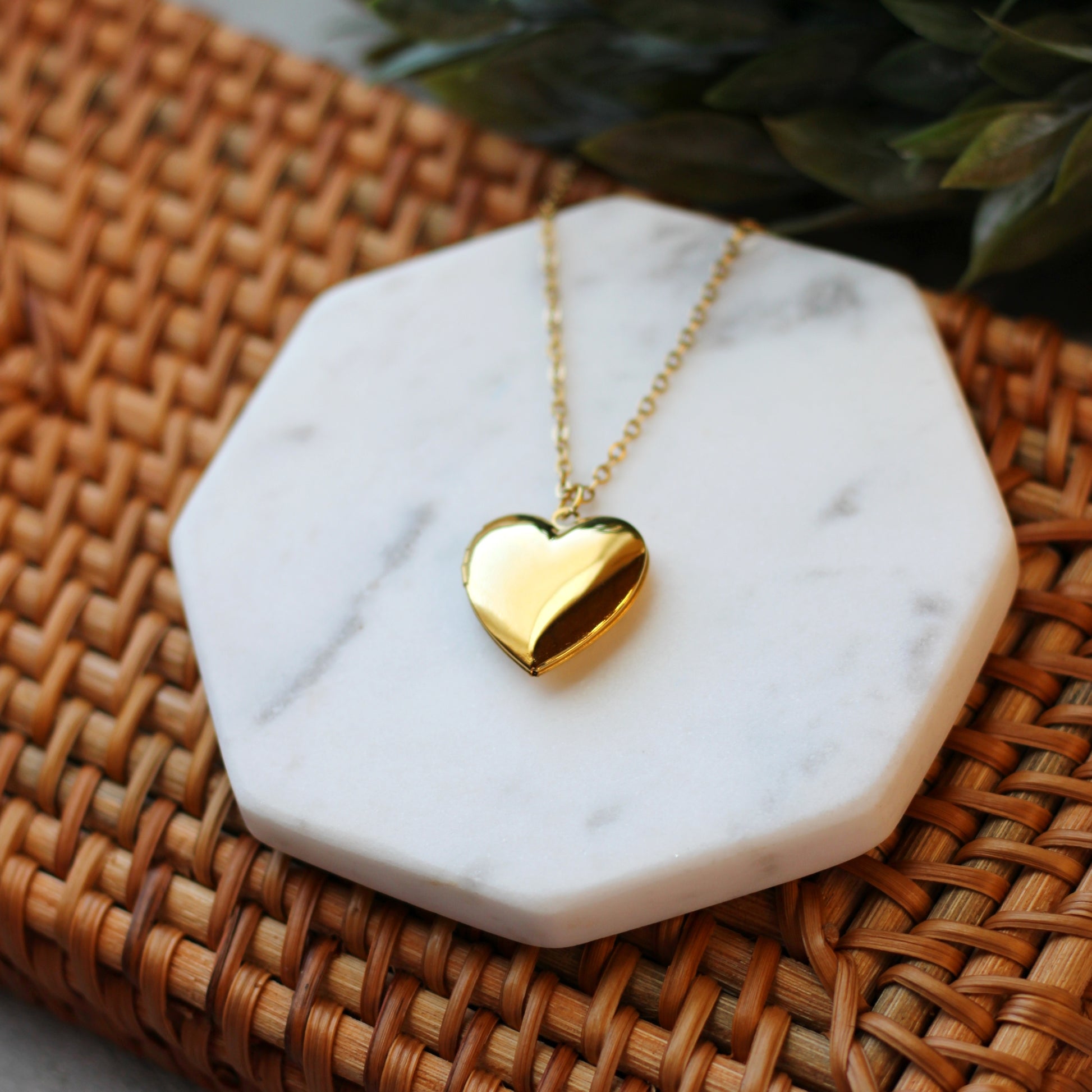 Gold heart-shaped necklace on a marble coaster with a woven surface background