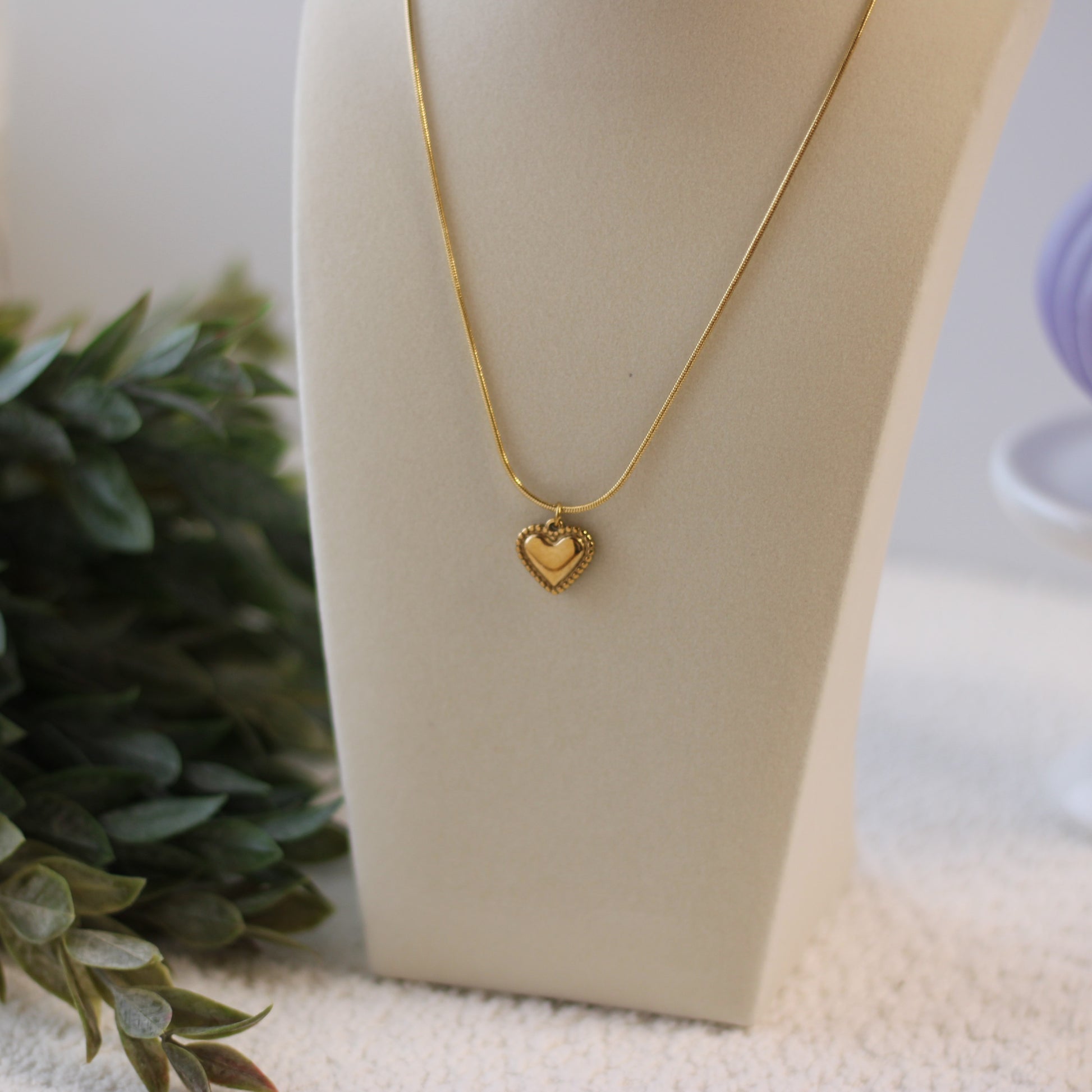 Gold heart-shaped necklace on a mannequin bust with a blurred background