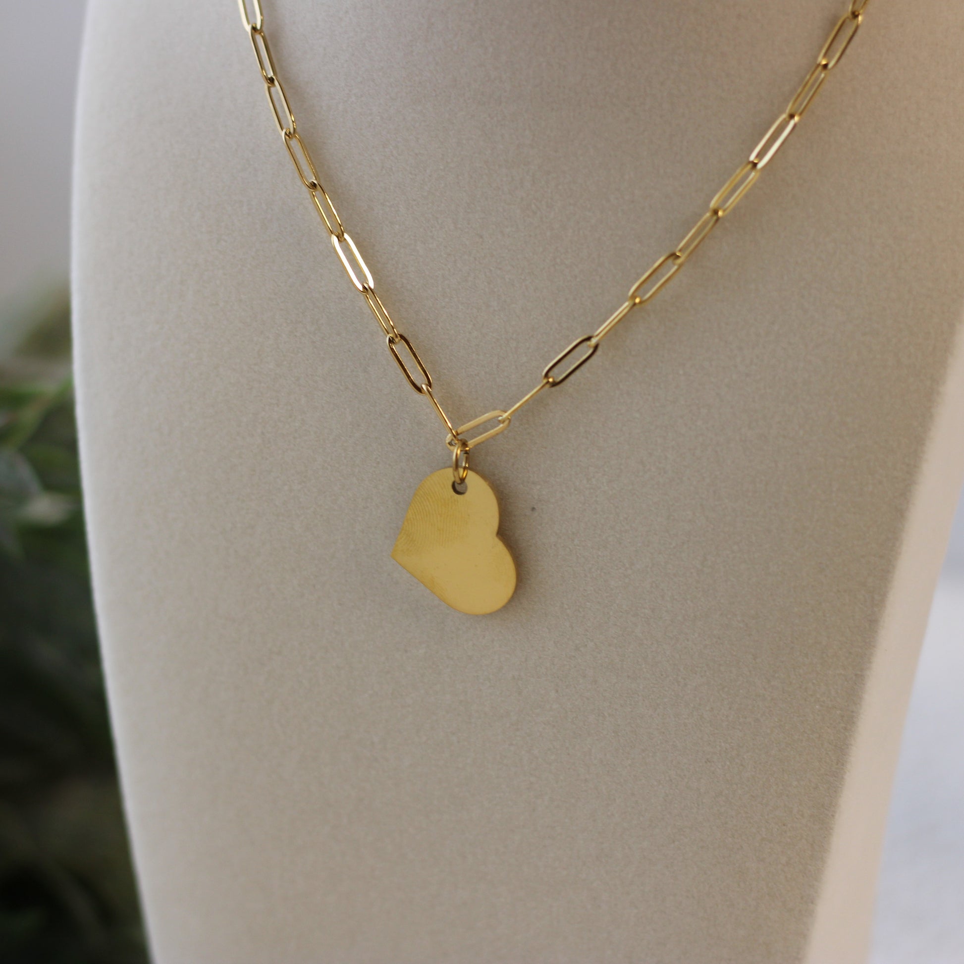Gold necklace with a heart-shaped pendant on a mannequin bust.
