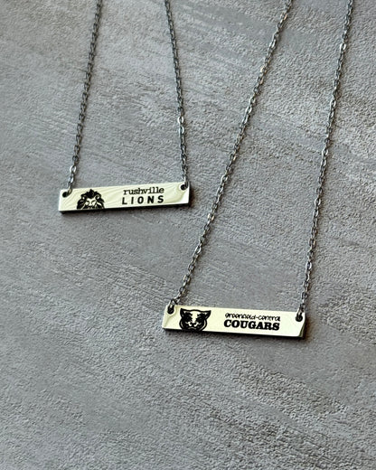Two silver bar necklaces with engraved text on a gray surface