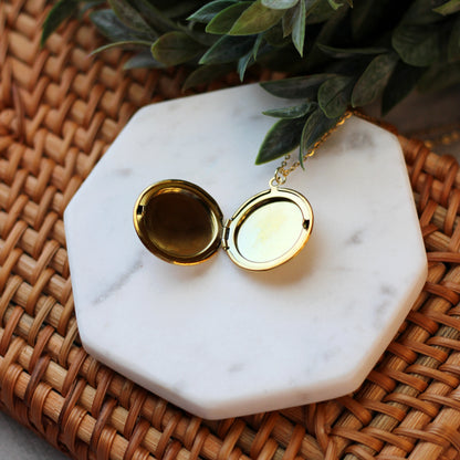 Gold locket on a marble coaster with a plant in the background