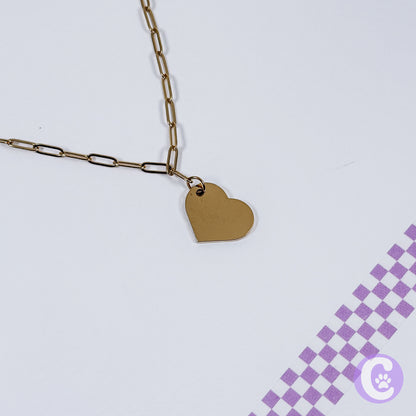 Gold heart-shaped pendant on a chain against a light purple background