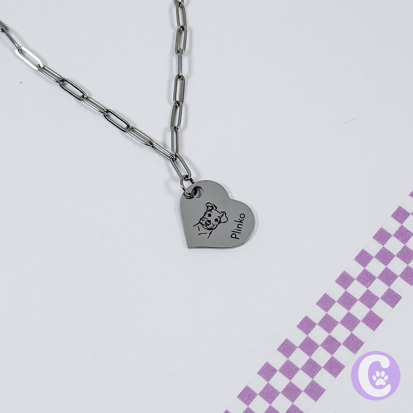 Heart-shaped pendant with engraved design on a chain against a light gray background