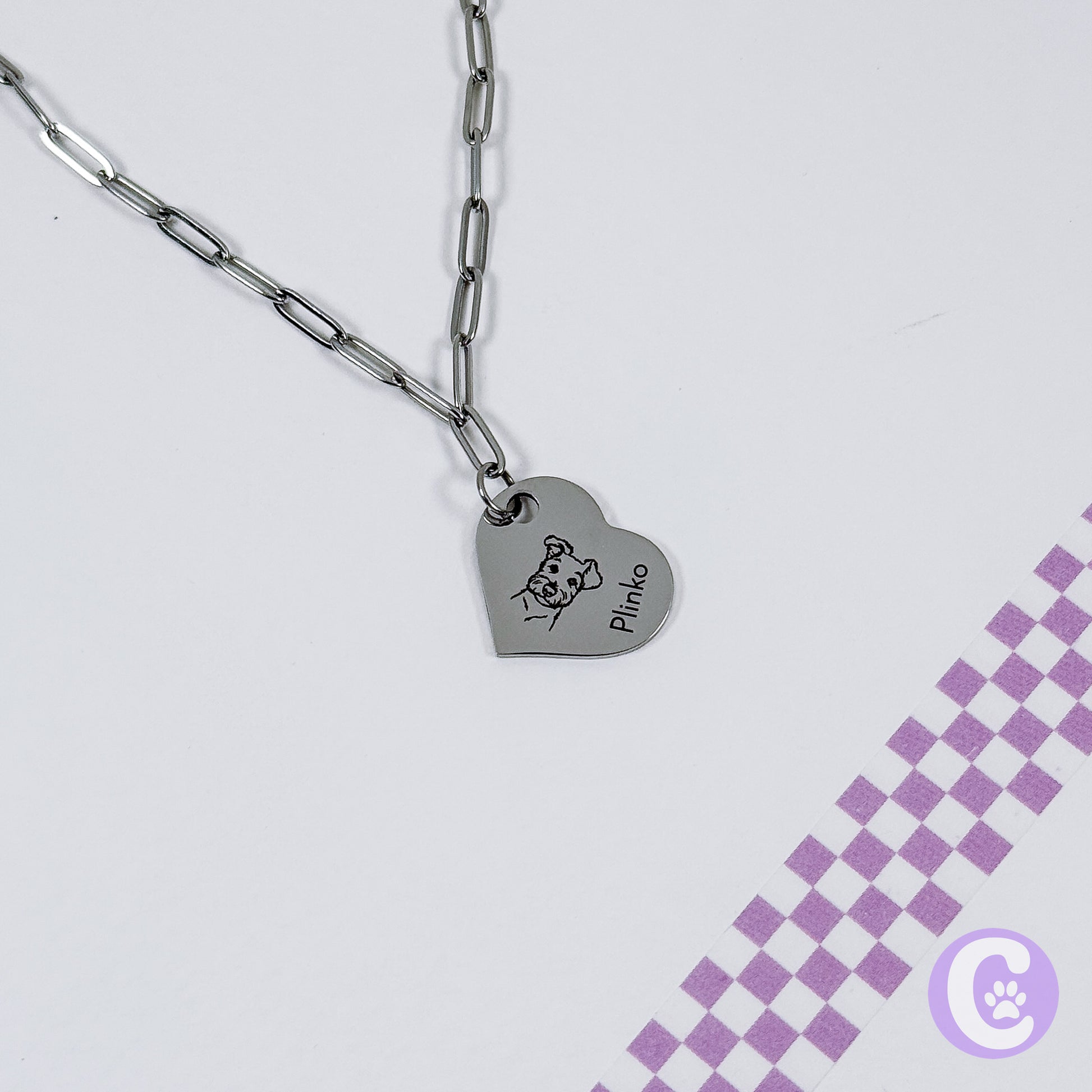 Heart-shaped pendant with engraved design on a chain against a light gray background