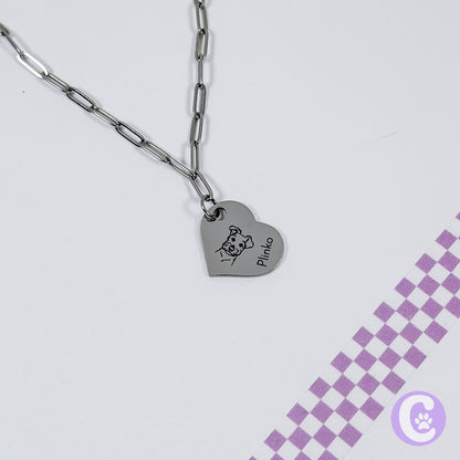 Heart-shaped pendant with engraved design on a chain against a light gray background