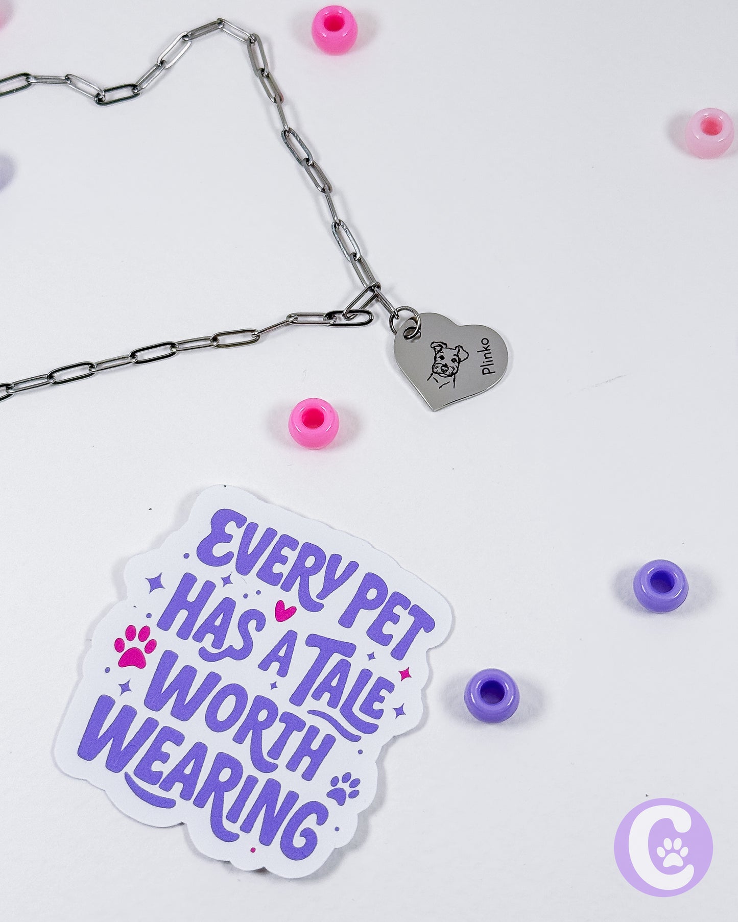 Sticker with 'Every pet has a tale worth wearing' text next to a chain and heart-shaped tag on a white background.