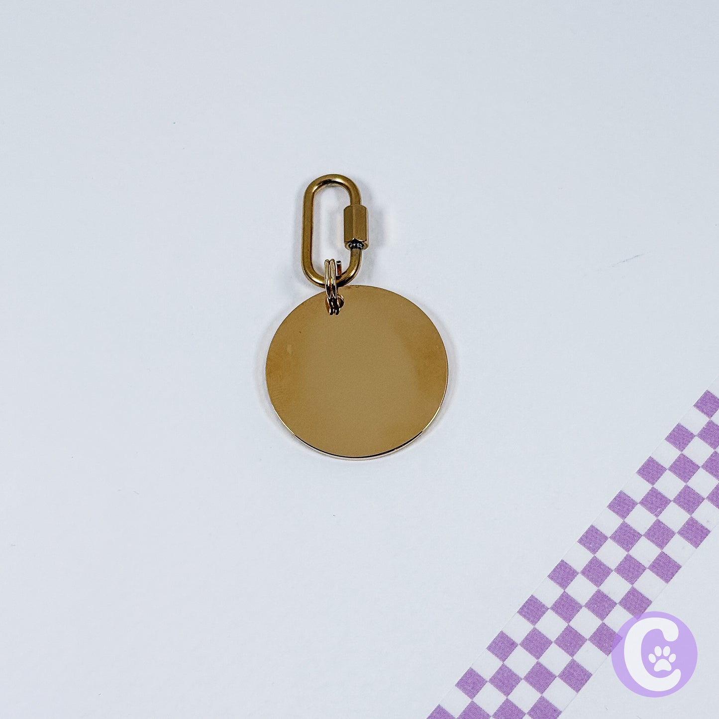 Gold round pendant with a carabiner on a light purple background