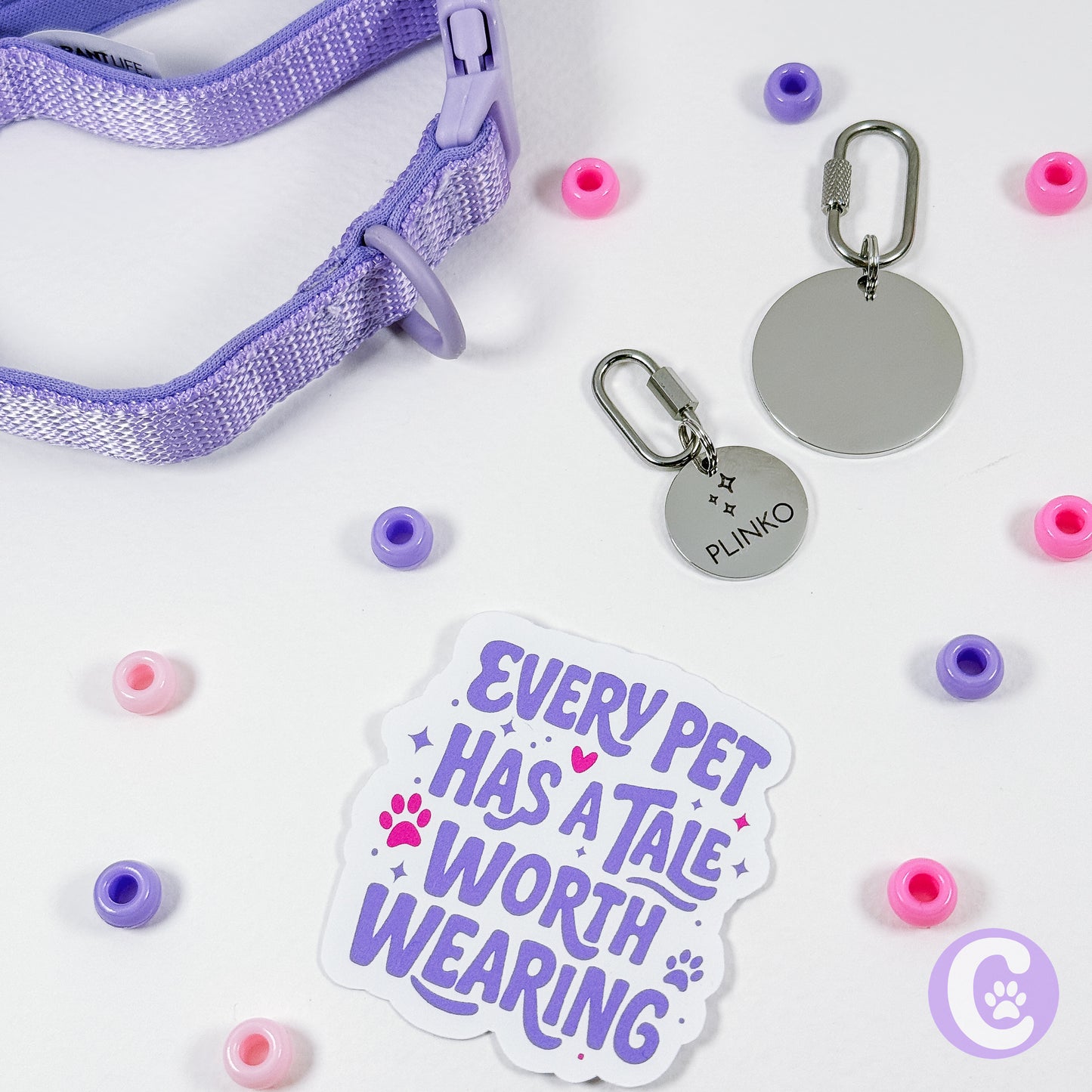 Pet accessories including a purple collar, tags, and a sticker with text on a white background.