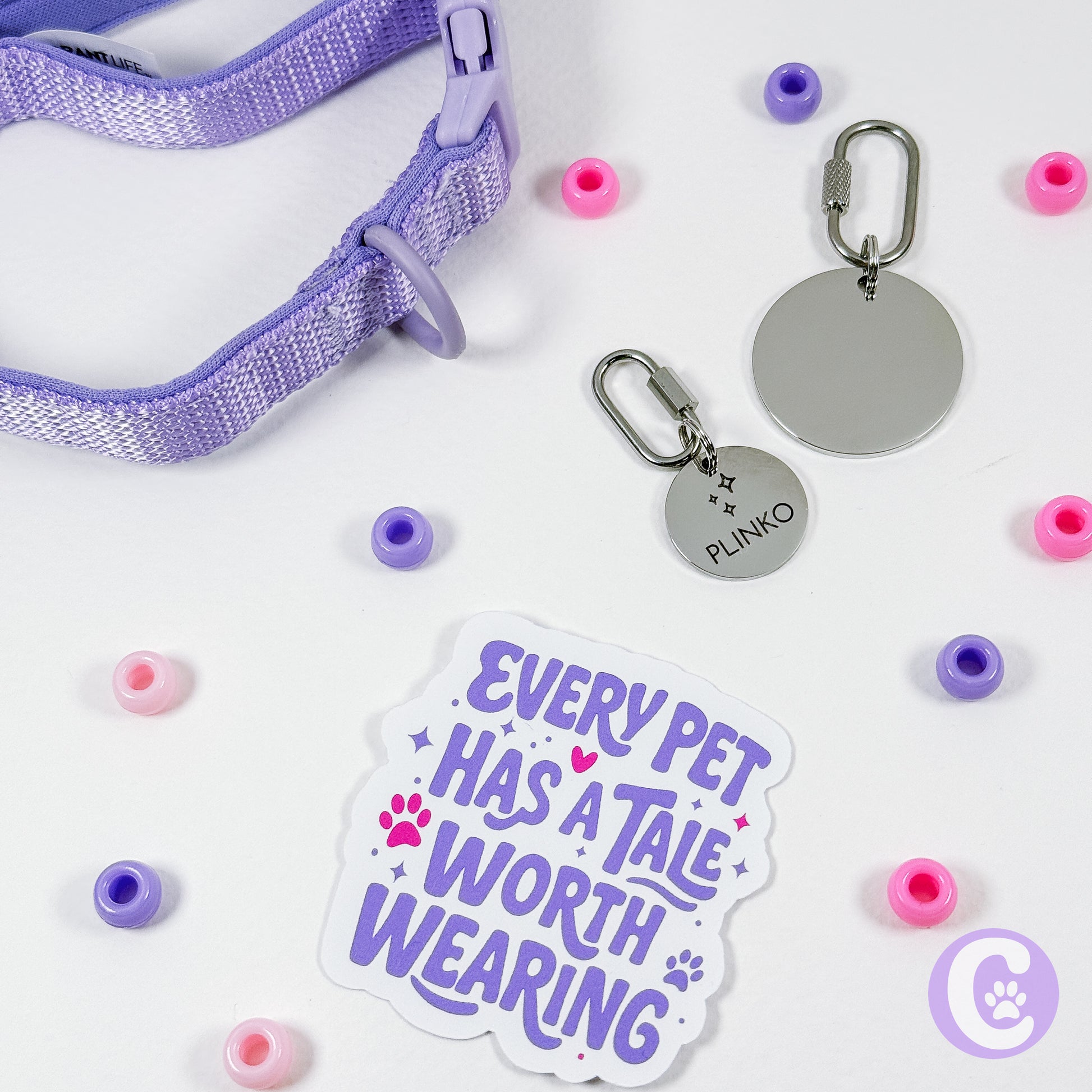Pet accessories including a purple collar, tags, and a sticker with text on a white background.