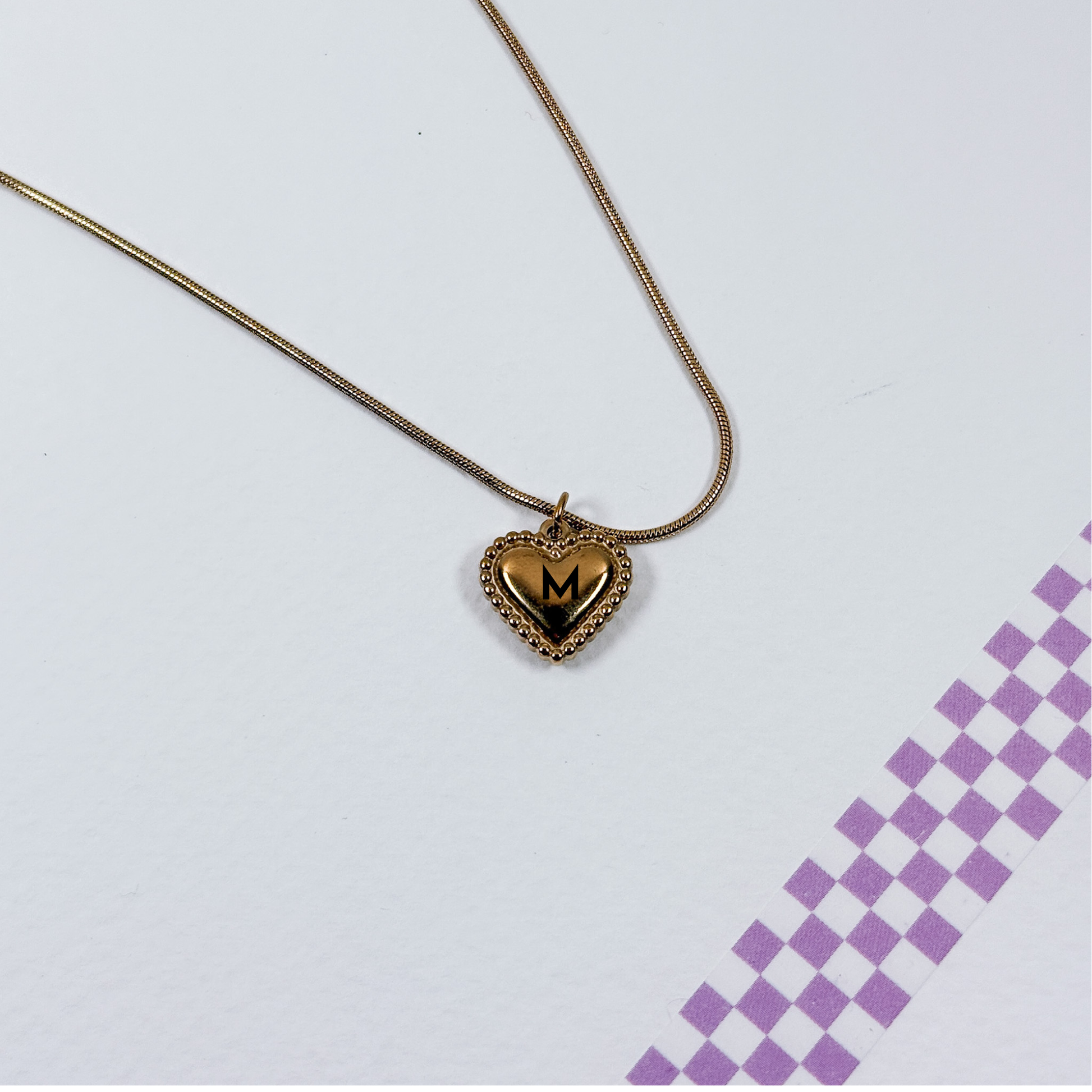 Gold heart-shaped necklace with a 'M' pendant on a light gray background