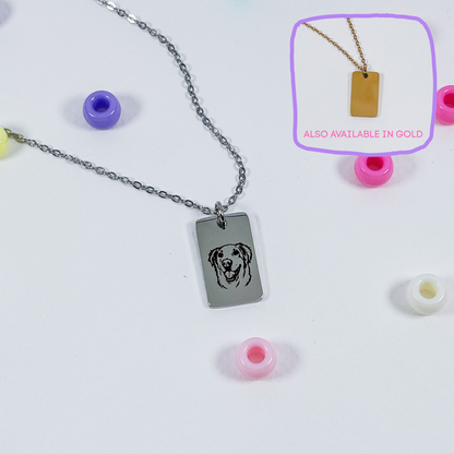 A silver rectangular pendant necklace with a dog face engraving, displayed on a white background with colorful beads. An inset in the top right shows the pendant on a gold chain with the text 'ALSO AVAILABLE IN GOLD'.