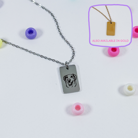 A silver rectangular pendant necklace with a dog face engraving, displayed on a white background with colorful beads. An inset in the top right shows the pendant on a gold chain with the text 'ALSO AVAILABLE IN GOLD'.