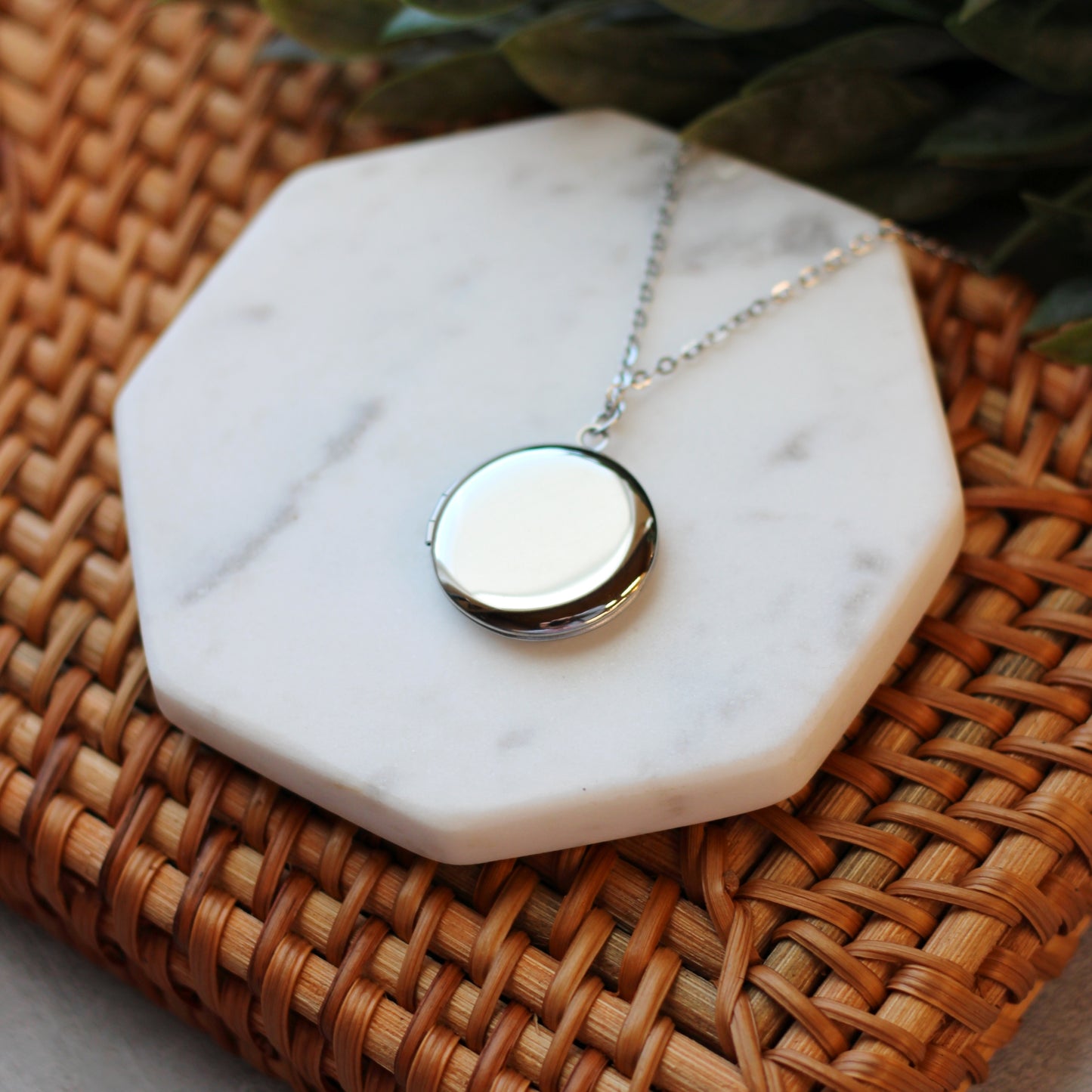 Necklace with a round pendant on a marble coaster on a woven surface