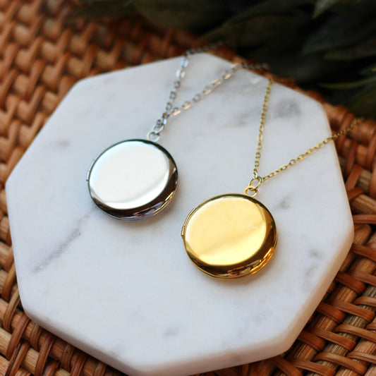 Two round necklaces, one gold and one silver, on a marble surface.