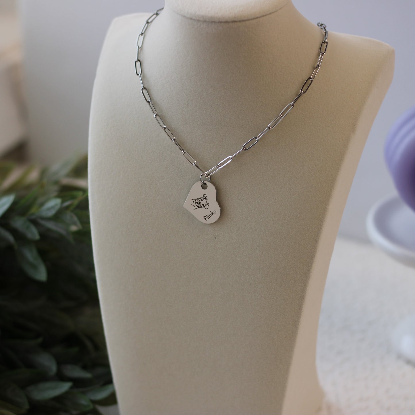 Silver necklace with a heart-shaped pendant on a mannequin bust.