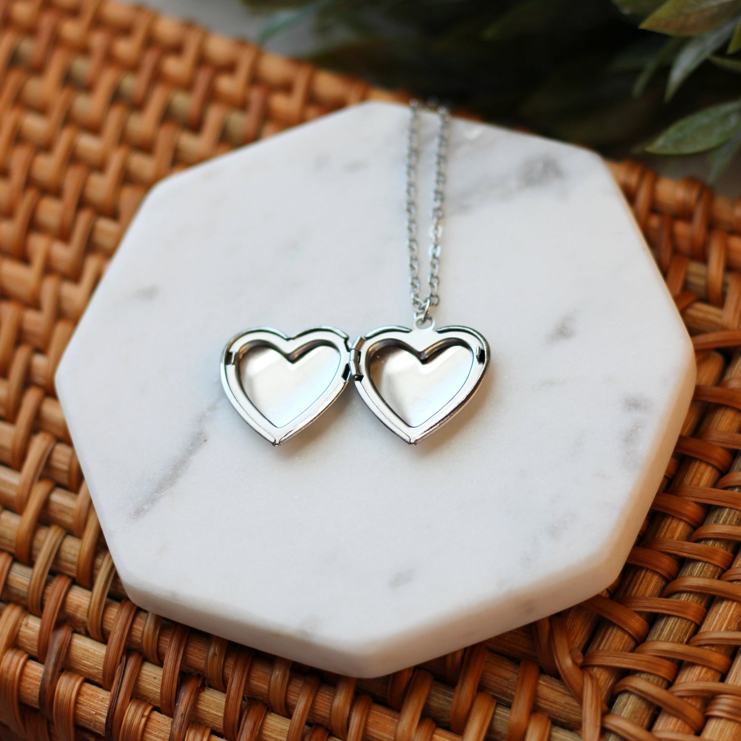 Silver heart-shaped pendant necklace on a marble coaster with a woven surface background