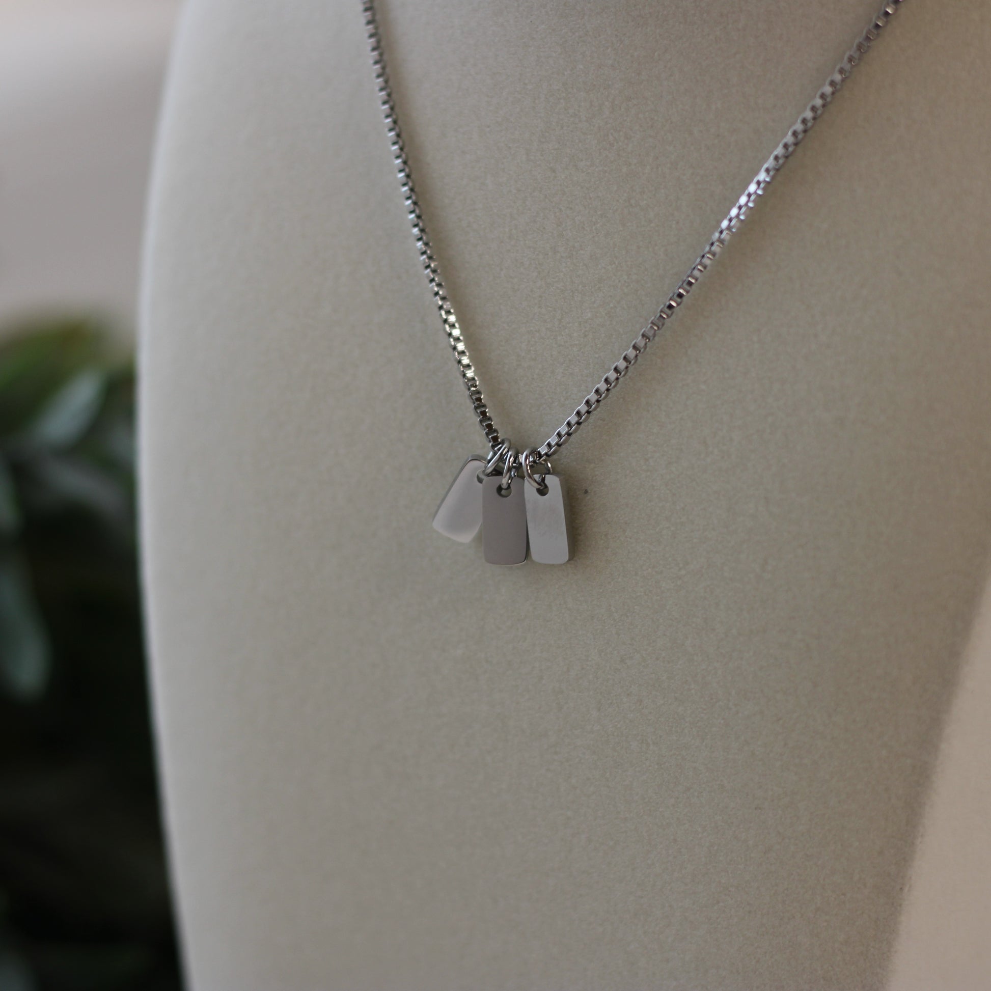 Silver necklace with three tags on a mannequin bust.