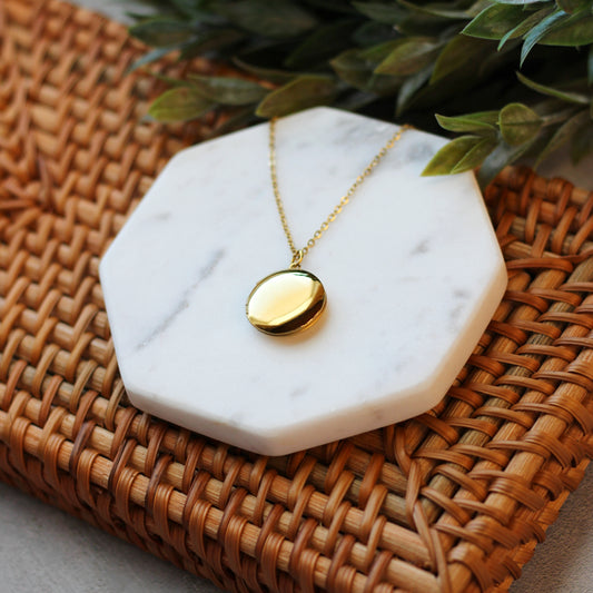 Gold necklace on a white marble coaster with a woven surface and green leaves in the background