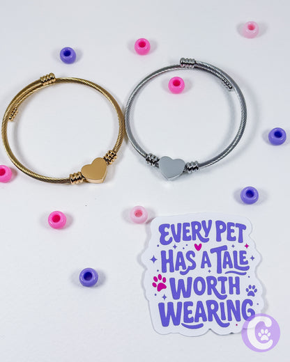 Two bracelets with heart-shaped clasps on a white background with decorative beads and a sticker reading 'Every pet has a tale worth wearing'.