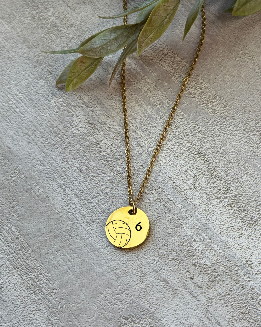 Gold necklace with a volleyball pendant on a textured surface